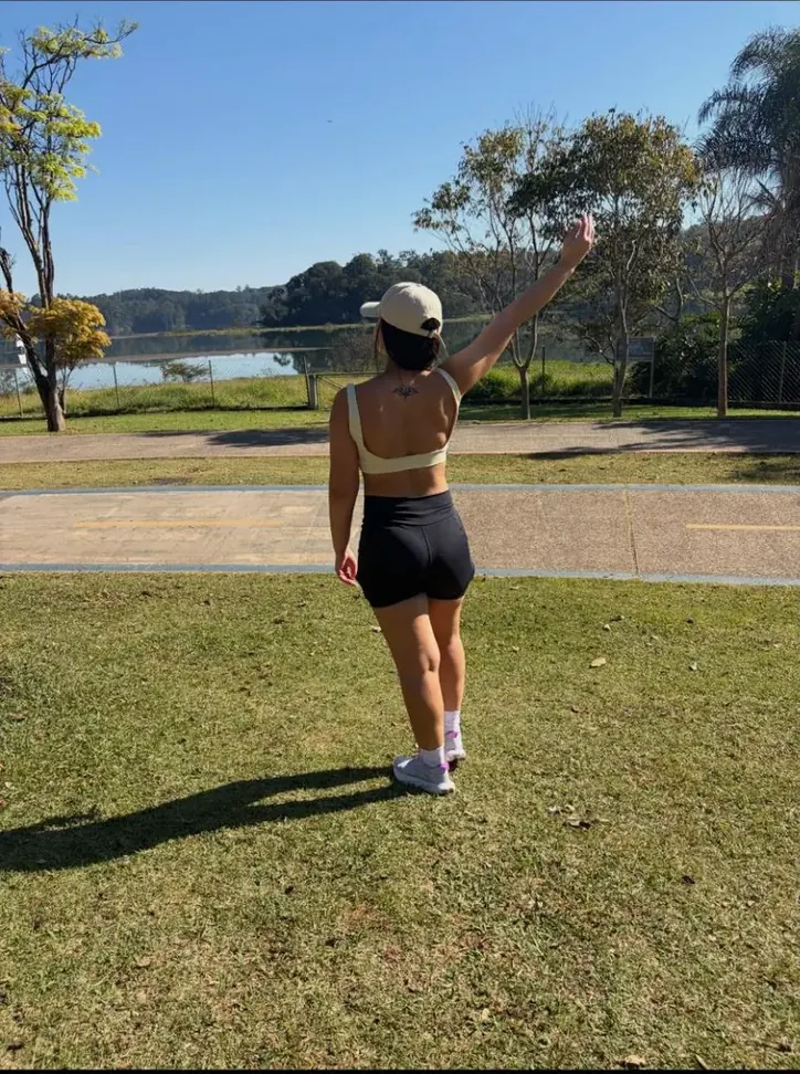 Gessica Gomes de costas, de boné e roupa de treino, num parque com lago